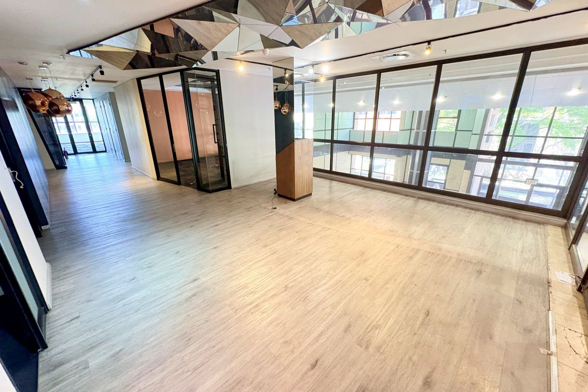 Spacious open-plan office area featuring modern laminate flooring, extensive glass partitioning, and a unique mirrored ceiling detail with integrated lighting.