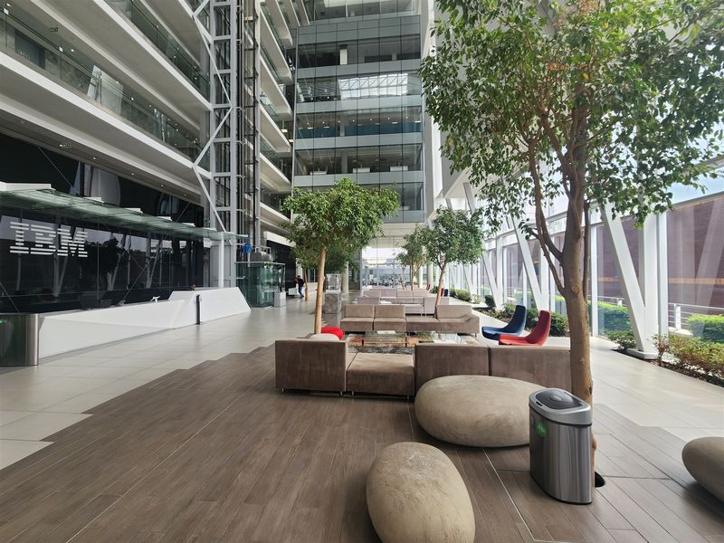 Spacious modern office atrium featuring high ceilings, glass facade, integrated reception area, and contemporary tiled flooring with indoor landscaping.