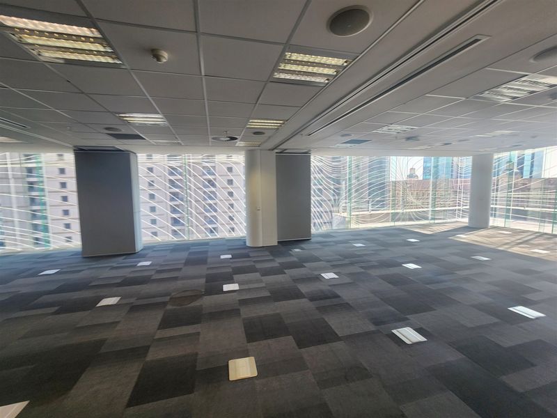 Spacious open-plan office area featuring suspended ceilings, recessed lighting, floor power boxes, and expansive floor-to-ceiling windows with city views.