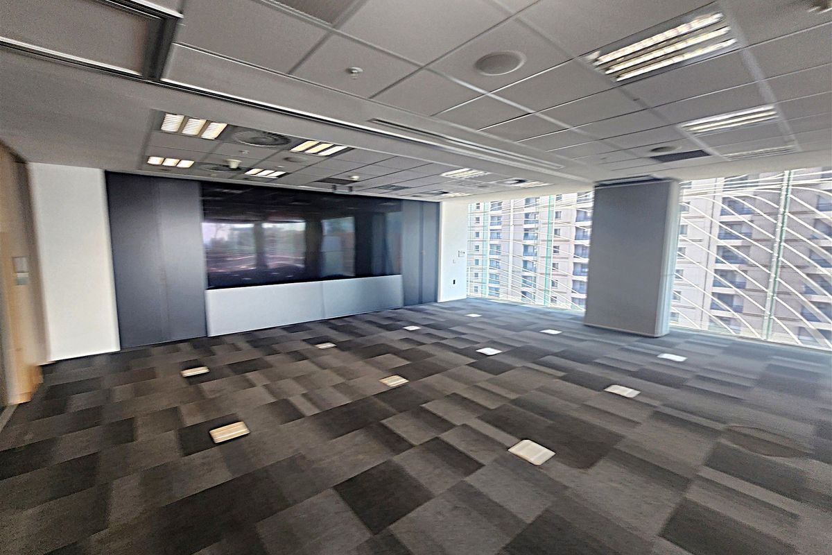 A spacious, empty office area featuring modern carpet tiles, a suspended ceiling with recessed lighting, and large windows providing ample natural light.
