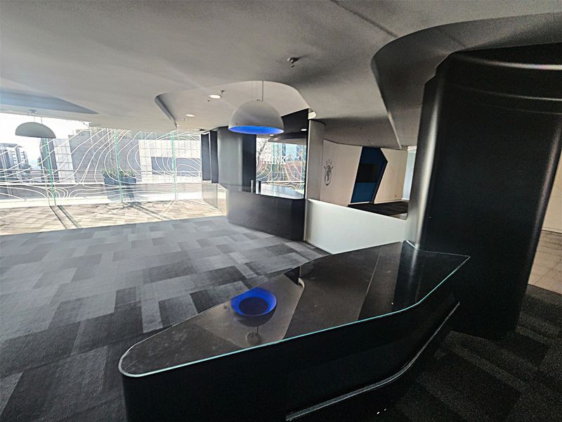 Modern open-plan office space featuring a sleek built-in reception desk, unique curved ceiling design, and large windows providing ample natural light.