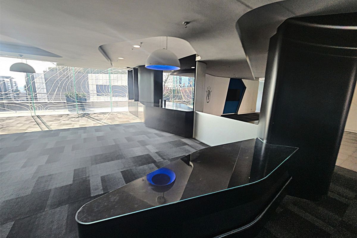 Modern open-plan office space featuring a sleek built-in reception desk, unique curved ceiling design, and large windows providing ample natural light.