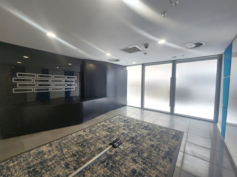 Modern office entrance area featuring a sleek built-in reception desk, tiled flooring, and large frosted glass doors providing natural light.