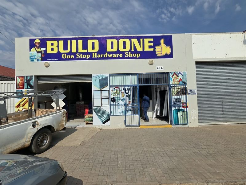 Front elevation of a commercial hardware shop featuring a roller shutter door, security gate, and paved frontage.