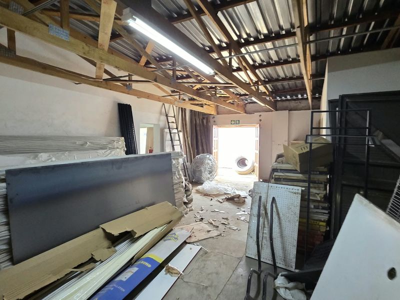 A large, unfinished utility or storage space featuring exposed timber roof trusses, corrugated metal roofing, and concrete flooring.