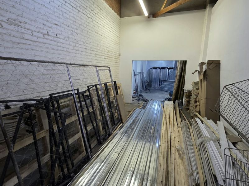 An unfinished utility or storage space featuring exposed brick walls, timber roof trusses, and basic fluorescent lighting, suitable for renovation or industrial use.