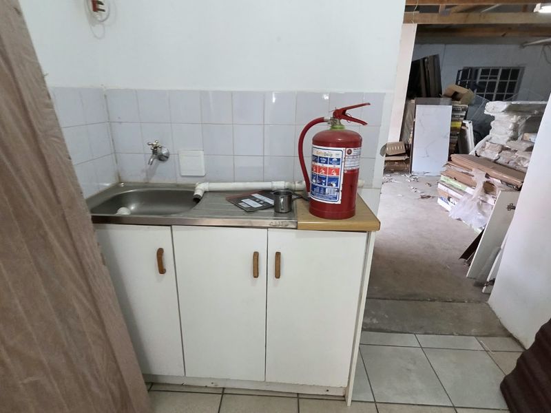 A basic utility area featuring a small stainless steel sink, built-in cabinetry, and tiled splashback, currently used for storage.