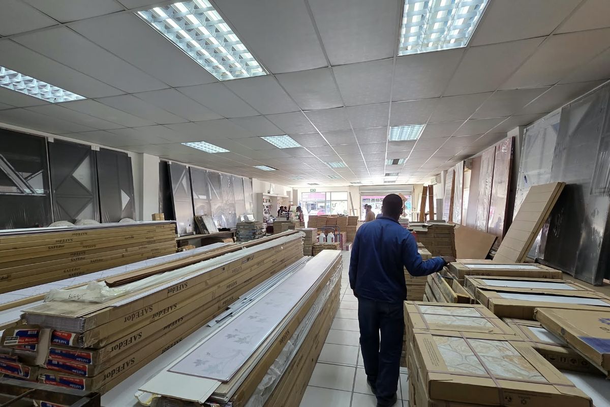 A commercial utility or warehouse space featuring a suspended ceiling with recessed lighting and tiled flooring, currently used for product storage.