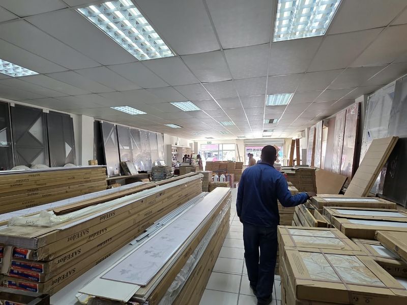 A commercial utility or warehouse space featuring a suspended ceiling with recessed lighting and tiled flooring, currently used for product storage.