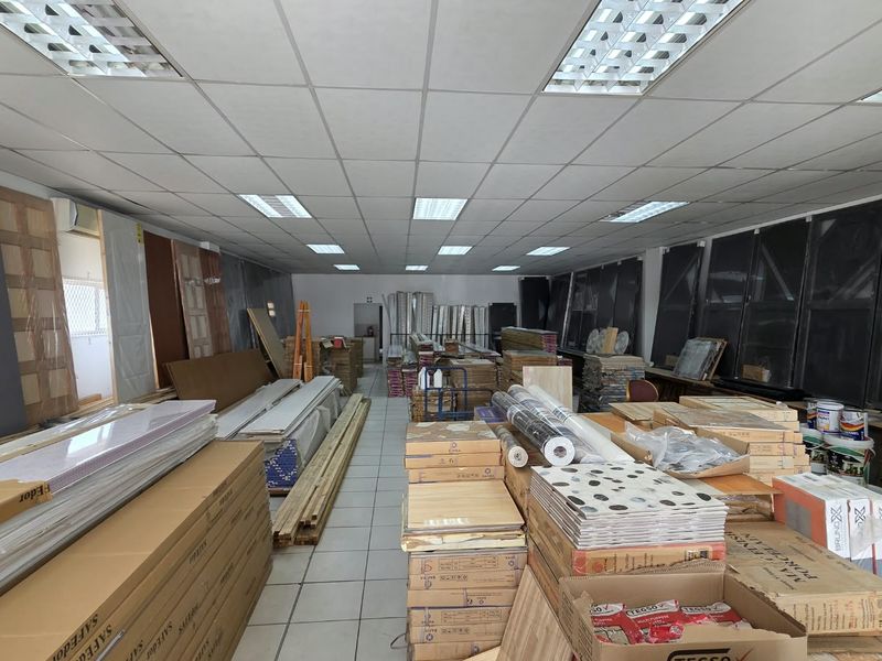 A commercial utility or storage space featuring a suspended ceiling with recessed lighting and tiled flooring, currently utilized for inventory storage.