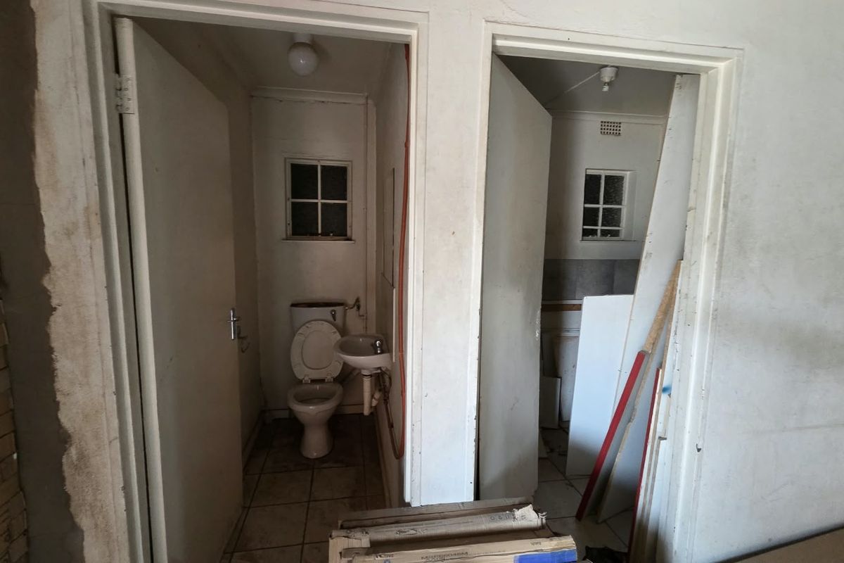 Two small bathroom cubicles featuring basic sanitary ware, tiled floors, and casement windows, currently in need of renovation and cosmetic updates.