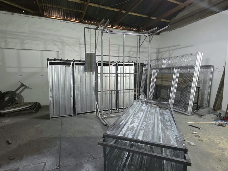 A large industrial utility space featuring concrete flooring and an exposed timber roof structure, currently used for metal fabrication and storage.