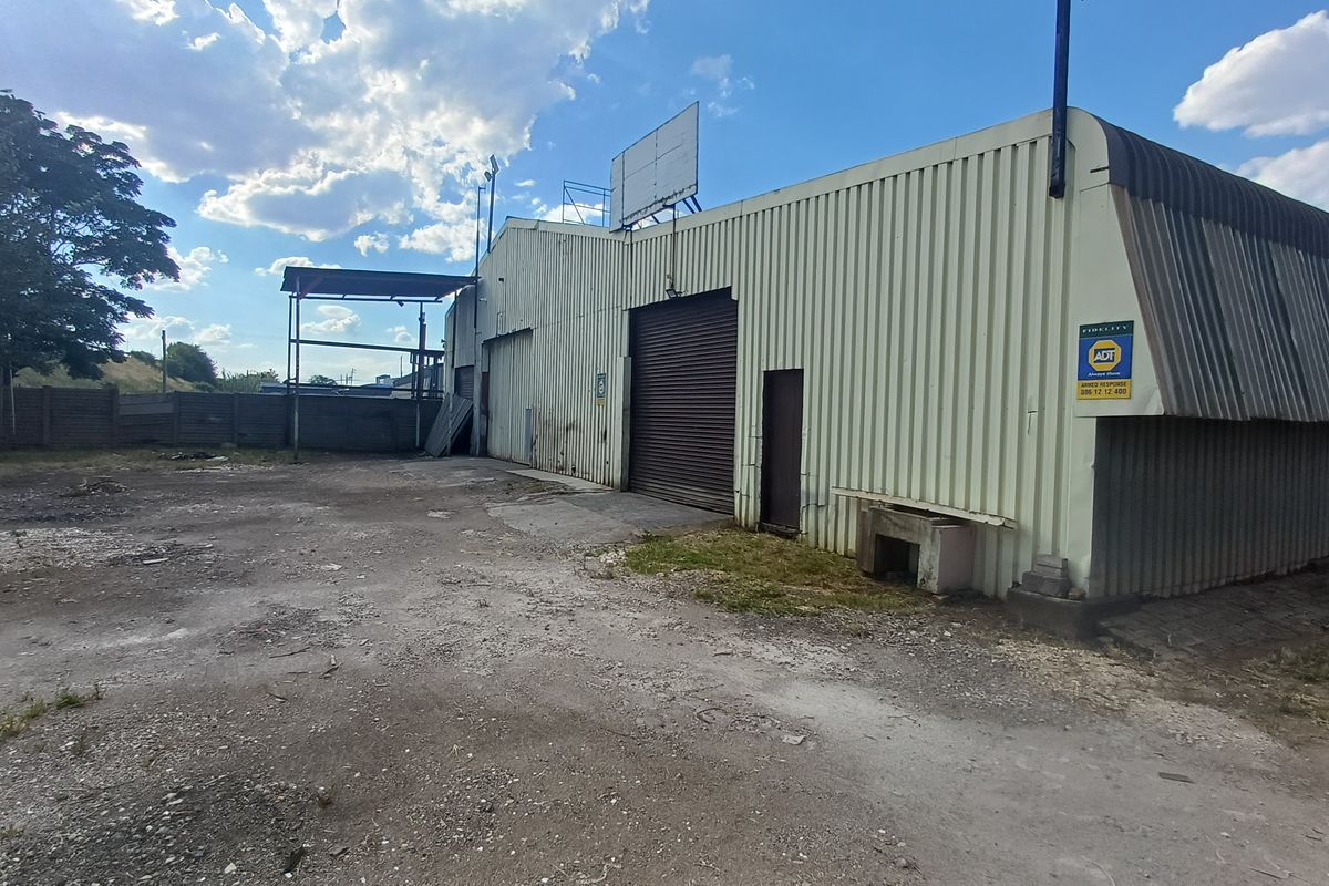 Industrial property exterior featuring corrugated metal cladding, a large roller shutter door, and an expansive unpaved yard area.