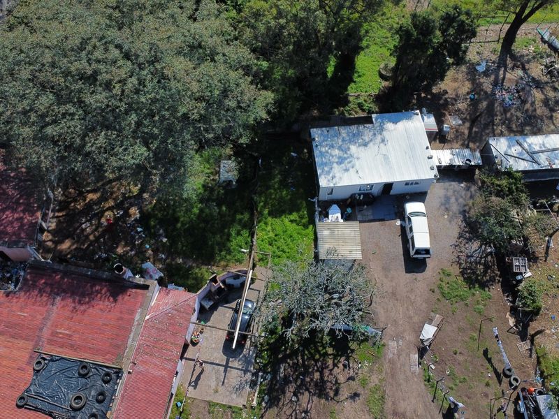 Aerial view of the farm property showing multiple structures with varied roofing, driveway access, and surrounding grounds requiring maintenance.