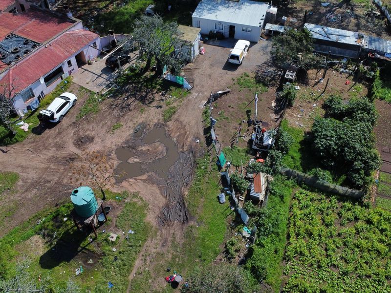 Aerial view of a farm property featuring multiple outbuildings, a water storage tank, and unpaved grounds with significant drainage issues.