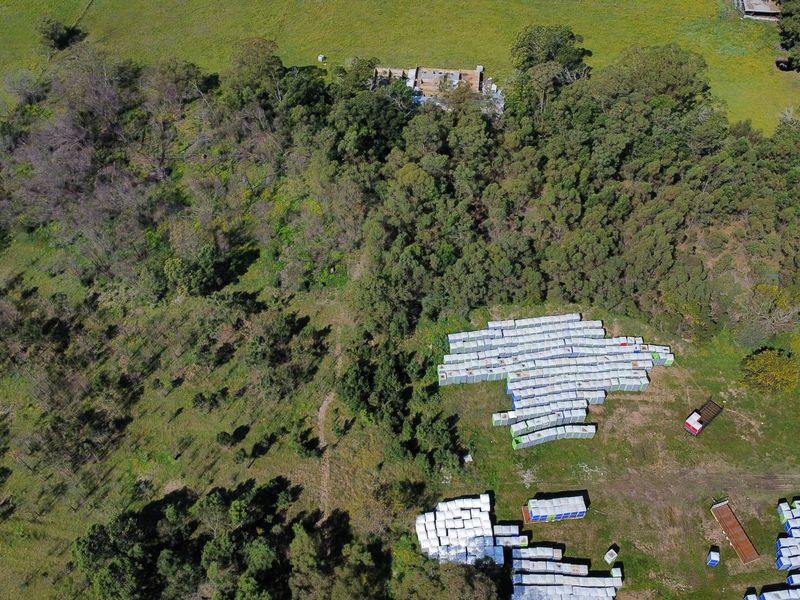 An aerial view of a large rural farm property featuring extensive open pasture, dense woodland areas, and a distant building structure.