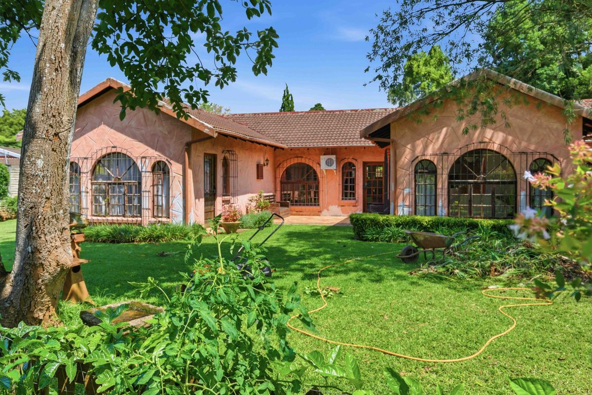 Rear view of a single-story property featuring a tiled roof, arched windows with security bars, and a well-maintained garden area.