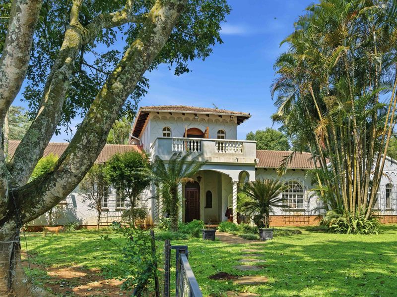 A charming double-story property featuring a classic architectural style, a balcony with stone balustrades, and a lush, well-established garden setting.