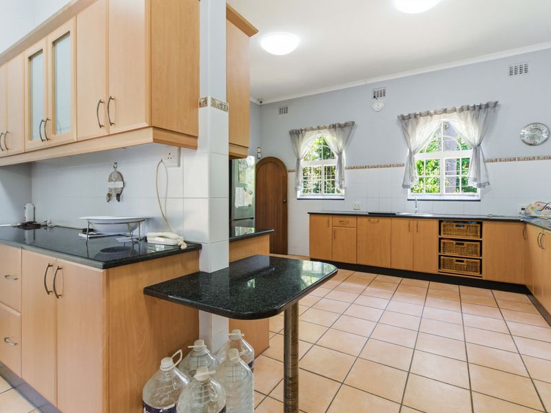 Spacious kitchen featuring light wood cabinetry, dark granite countertops, tiled flooring, and ample natural light through arched windows.