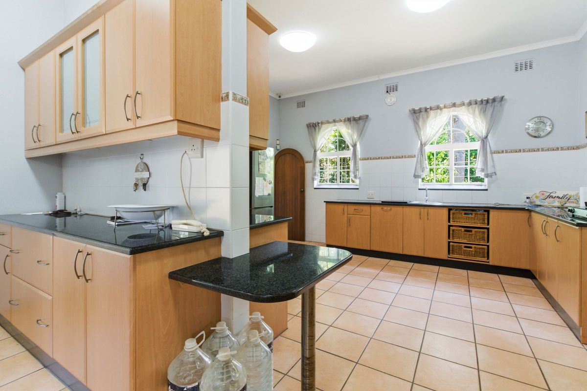 Spacious kitchen featuring light wood cabinetry, dark granite countertops, tiled flooring, and ample natural light through arched windows.