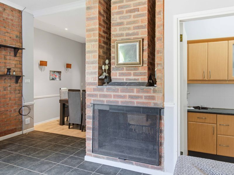Open plan living area featuring a central exposed brick fireplace, tiled and laminate flooring, and a functional kitchen area with built-in cabinetry.