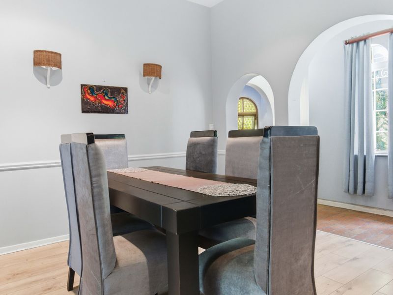 A dining room featuring arched architectural doorways, wall sconces, chair rail molding, and light-toned laminate flooring.