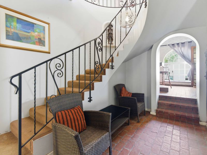 Welcoming entrance hall featuring a classic wrought iron staircase, terracotta tile flooring, and an arched transition leading to an adjacent space.
