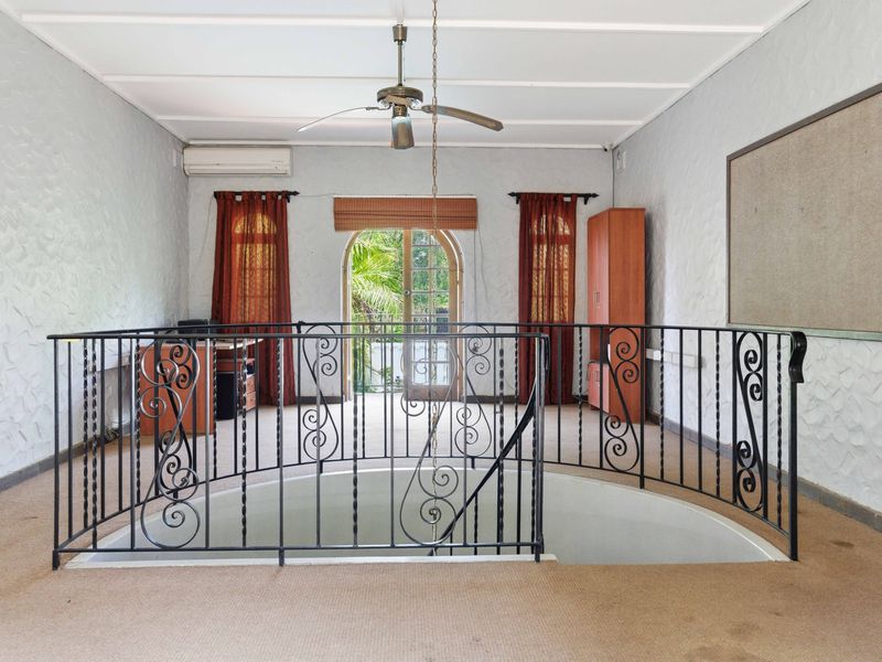 Upper level landing area featuring a wrought iron balustrade, carpeted flooring, and access to an exterior balcony through an arched glass door.