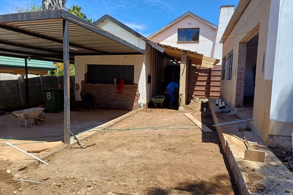 Exterior view of a commercial property undergoing active construction and renovation, featuring a metal carport structure and exposed building foundations.