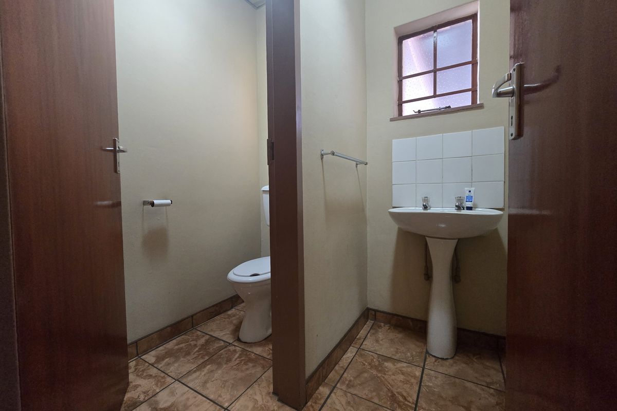 A functional commercial restroom featuring a pedestal basin with tiled splashback and a separate toilet cubicle with tiled flooring.