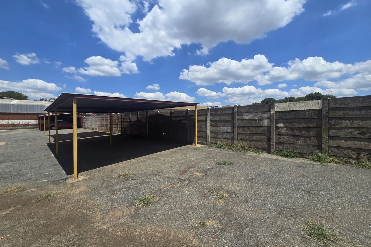 Outdoor parking area featuring a covered steel carport structure and a concrete perimeter boundary wall.