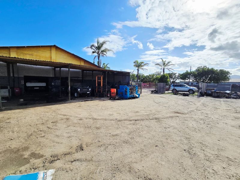 Industrial property featuring a large open dirt yard and a covered workspace area with a metal roof structure.