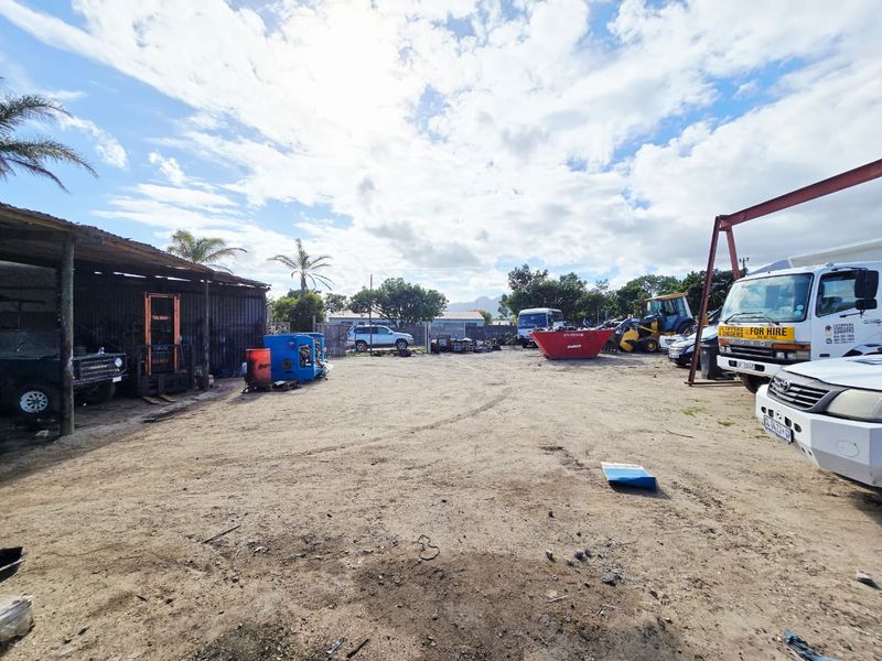 Industrial yard space featuring a corrugated iron shed structure and an overhead gantry crane frame, suitable for heavy equipment storage or industrial operations.