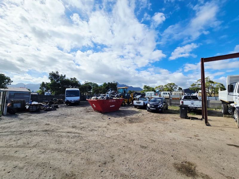 An expansive, unpaved industrial yard area enclosed by a perimeter wall, featuring a steel structural beam and ample open space for storage or operations.