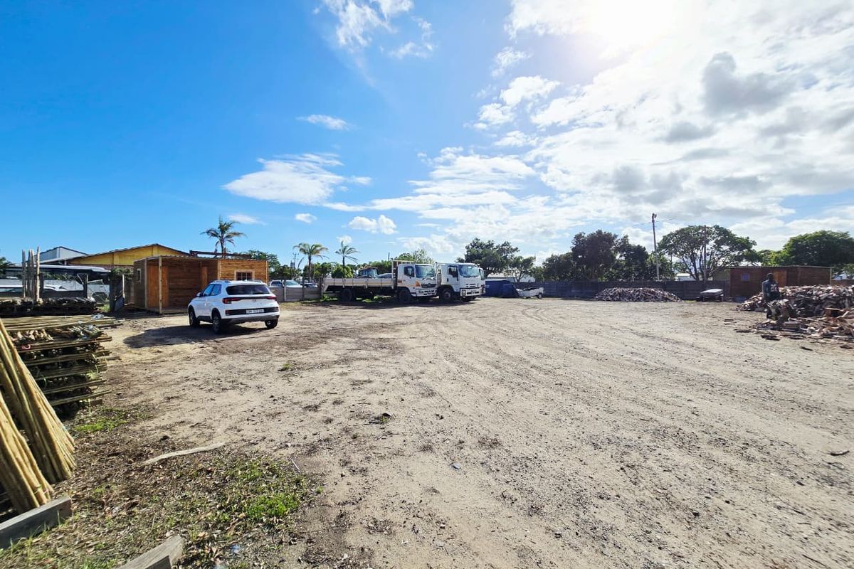 A wide-angle view of an industrial yard featuring an unpaved surface, perimeter fencing, and open storage space.