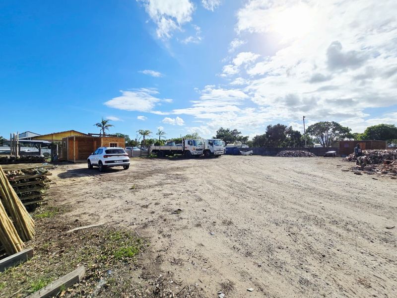 A wide-angle view of an industrial yard featuring an unpaved surface, perimeter fencing, and open storage space.