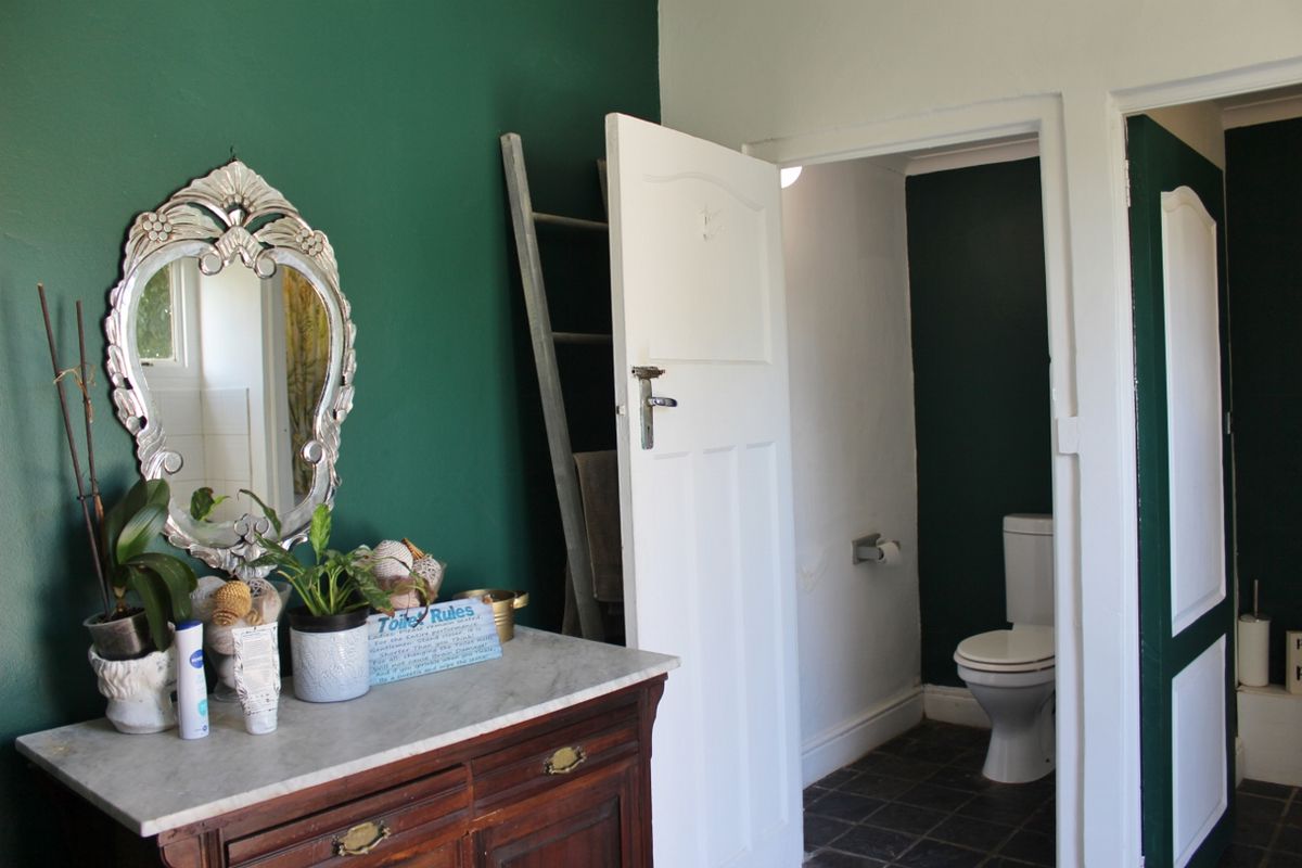A bathroom featuring a marble-topped vanity and a separate toilet area with dark green accent walls and tiled flooring.