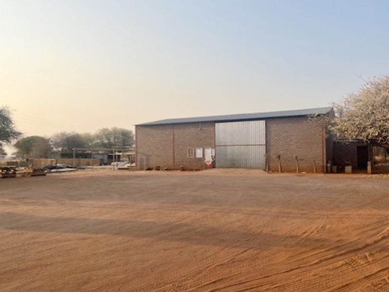 Industrial warehouse building featuring a face brick facade, large sliding metal door, and a spacious gravel yard area.