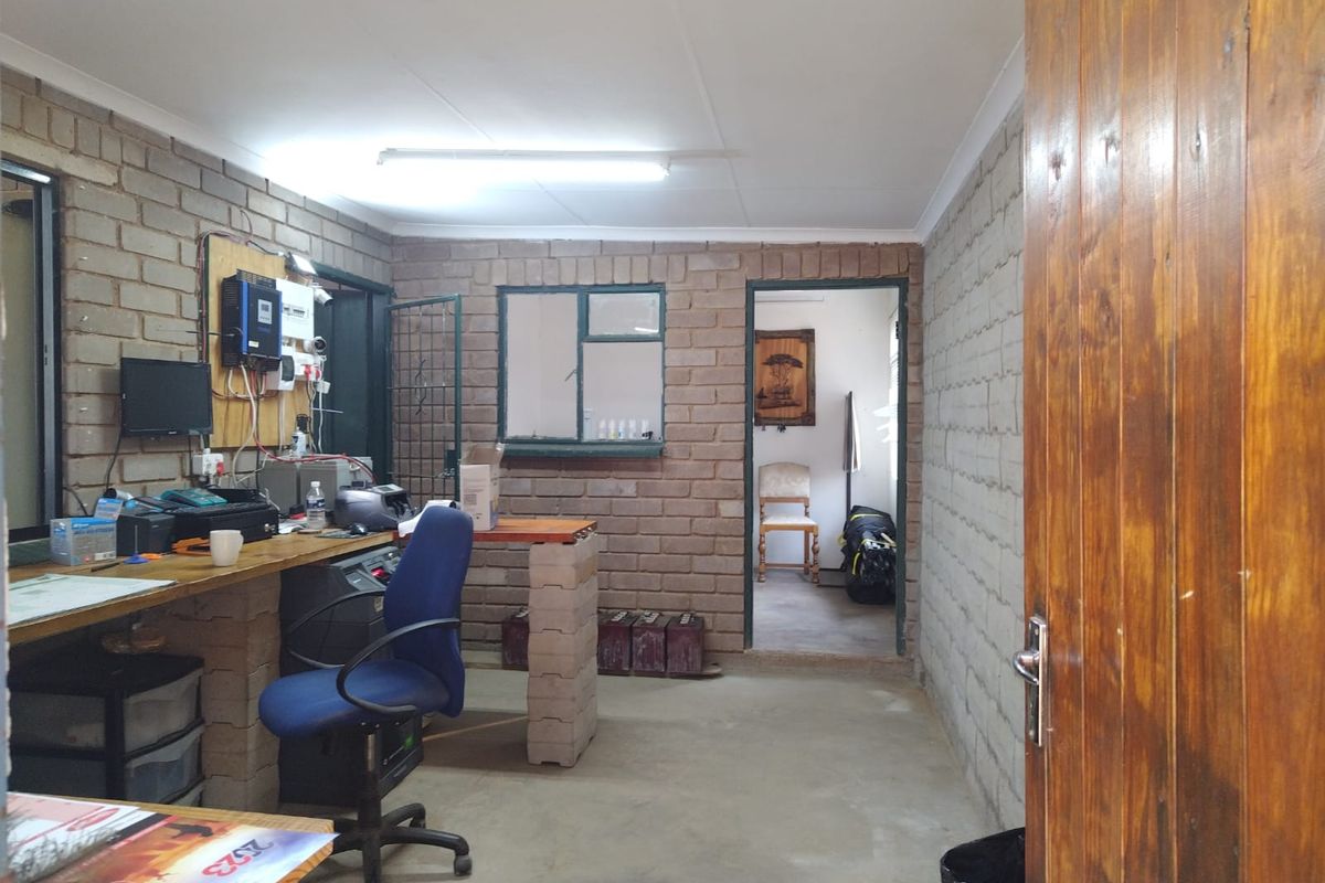 Functional industrial office space featuring exposed brick walls, built-in workbench, and direct access to an adjacent room.