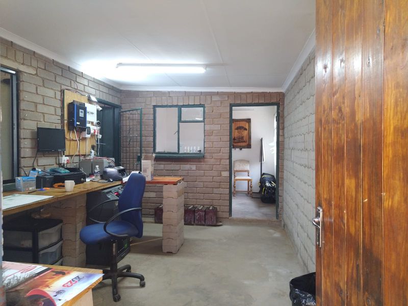 Functional industrial office space featuring exposed brick walls, built-in workbench, and direct access to an adjacent room.