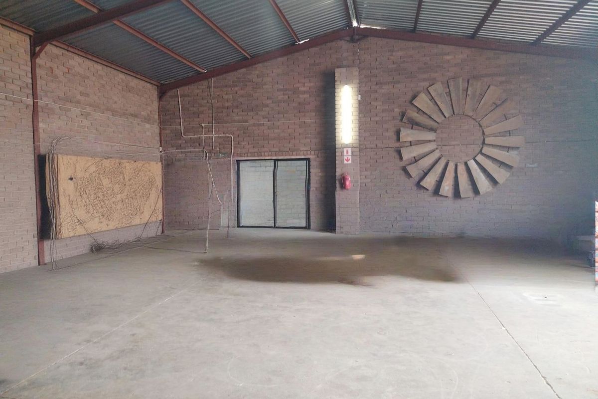 Spacious industrial utility area featuring exposed brick walls, concrete flooring, and high-clearance corrugated metal roofing with integrated lighting and fire safety equipment.
