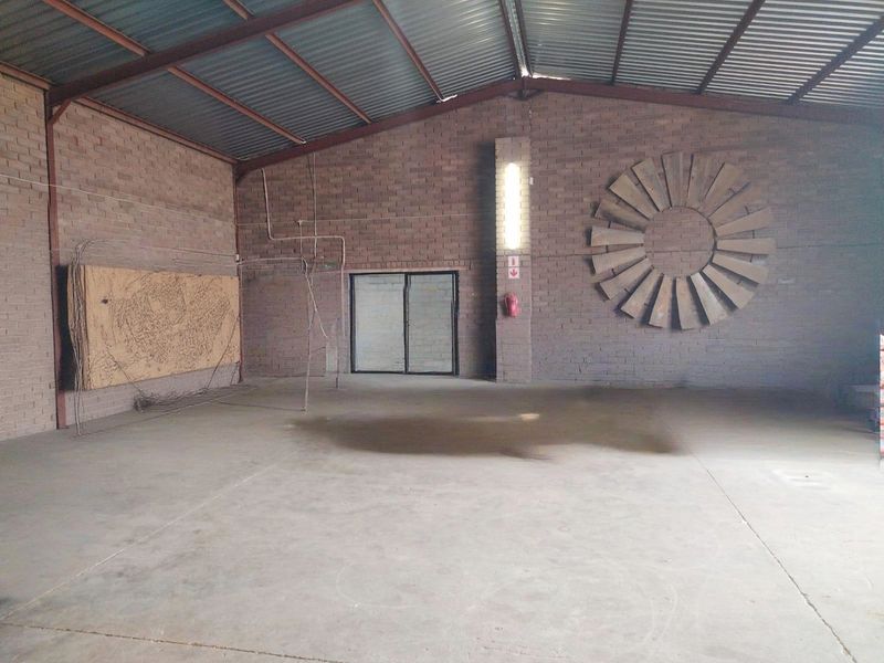 Spacious industrial utility area featuring exposed brick walls, concrete flooring, and high-clearance corrugated metal roofing with integrated lighting and fire safety equipment.