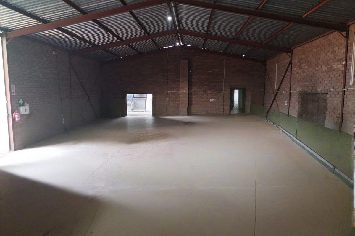 Spacious industrial warehouse unit featuring exposed brick walls, high-clearance steel roof trusses, and durable concrete flooring, suitable for various commercial or storage applications.