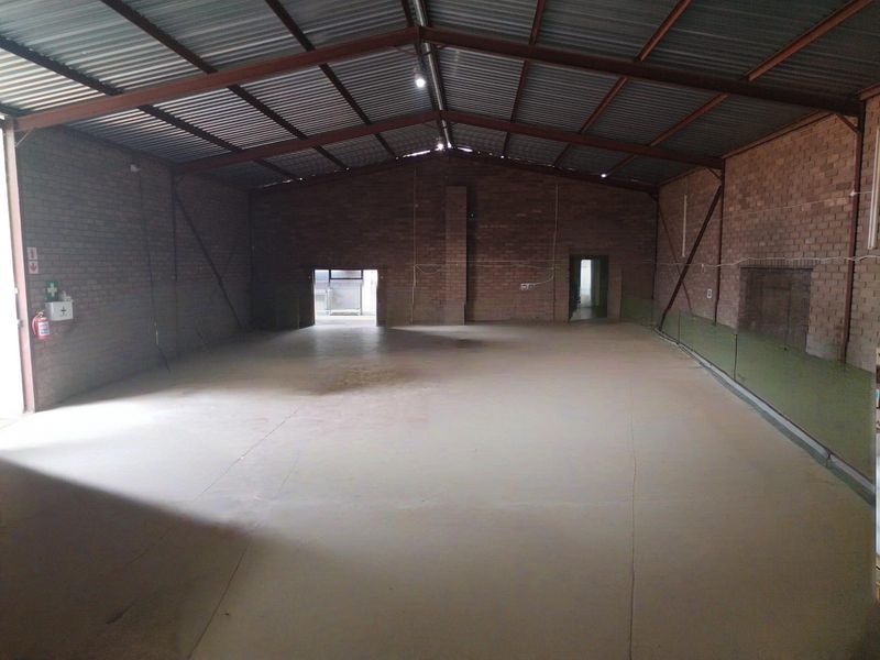 Spacious industrial warehouse unit featuring exposed brick walls, high-clearance steel roof trusses, and durable concrete flooring, suitable for various commercial or storage applications.