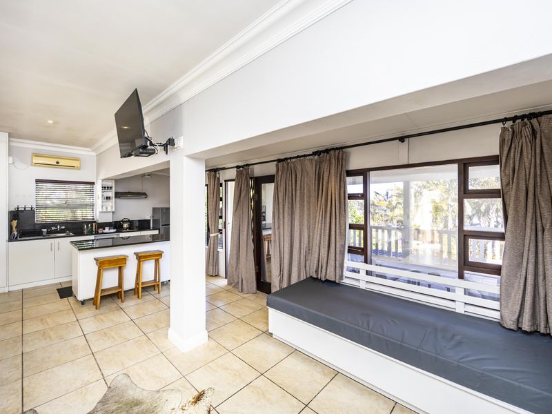 Open-plan living and kitchen area featuring tiled floors, a breakfast bar, built-in window seating, and direct access to an outdoor patio.
