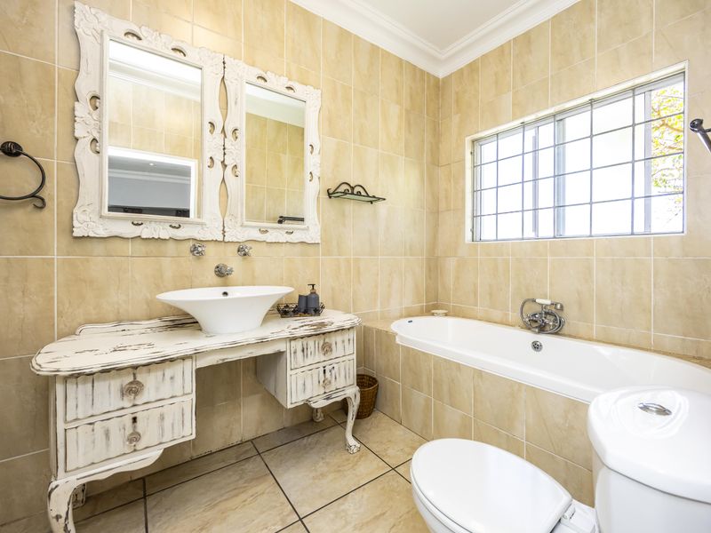 A well-maintained bathroom featuring neutral ceramic tiling, a built-in bathtub, a wall-mounted basin, and a window with security bars.