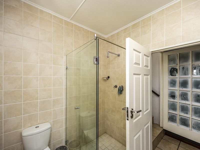 A functional bathroom featuring a glass-enclosed shower, tiled walls, and a standard toilet, with direct access to an adjacent hallway.