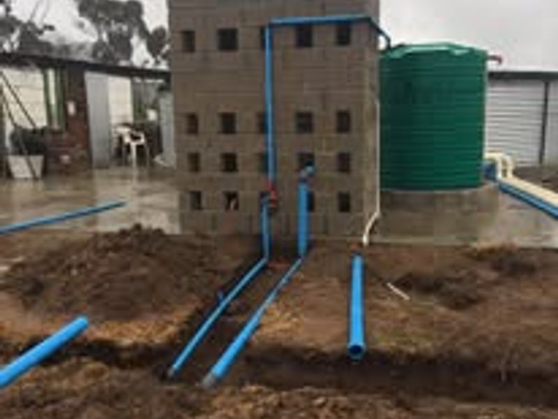 Utility area featuring a water storage tank and concrete block structure with exposed plumbing and ongoing ground trenching works.