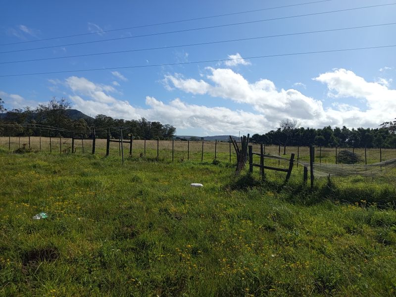 An expansive open field on a farm property featuring wire fencing and wooden posts with distant mountain views.
