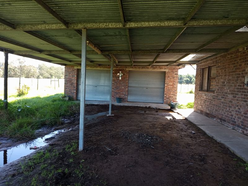 A detached brick garage structure featuring two roller shutter doors and a corrugated metal roof, situated on an unpaved farm yard area.